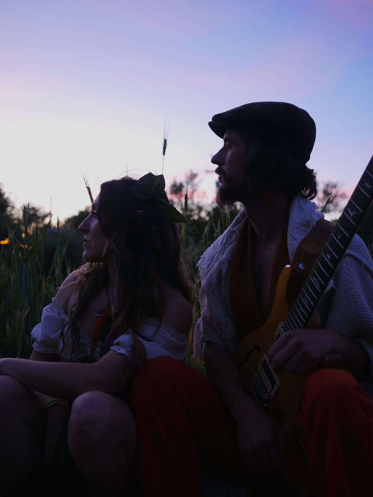 Bexx Rosenbloom and Travis Puntarelli in silhouette against an evening sky, guitar in hand