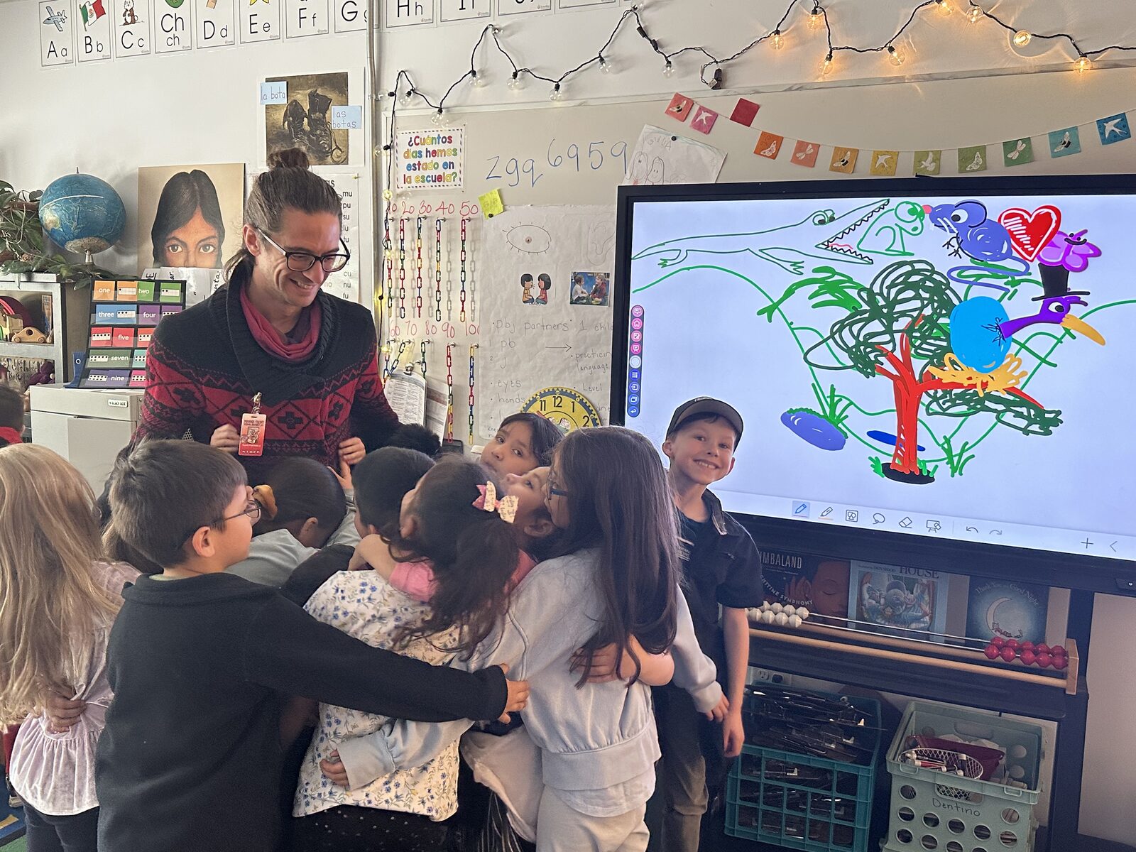 Travis surrounded by students for a group hug, classroom smartboard behind them