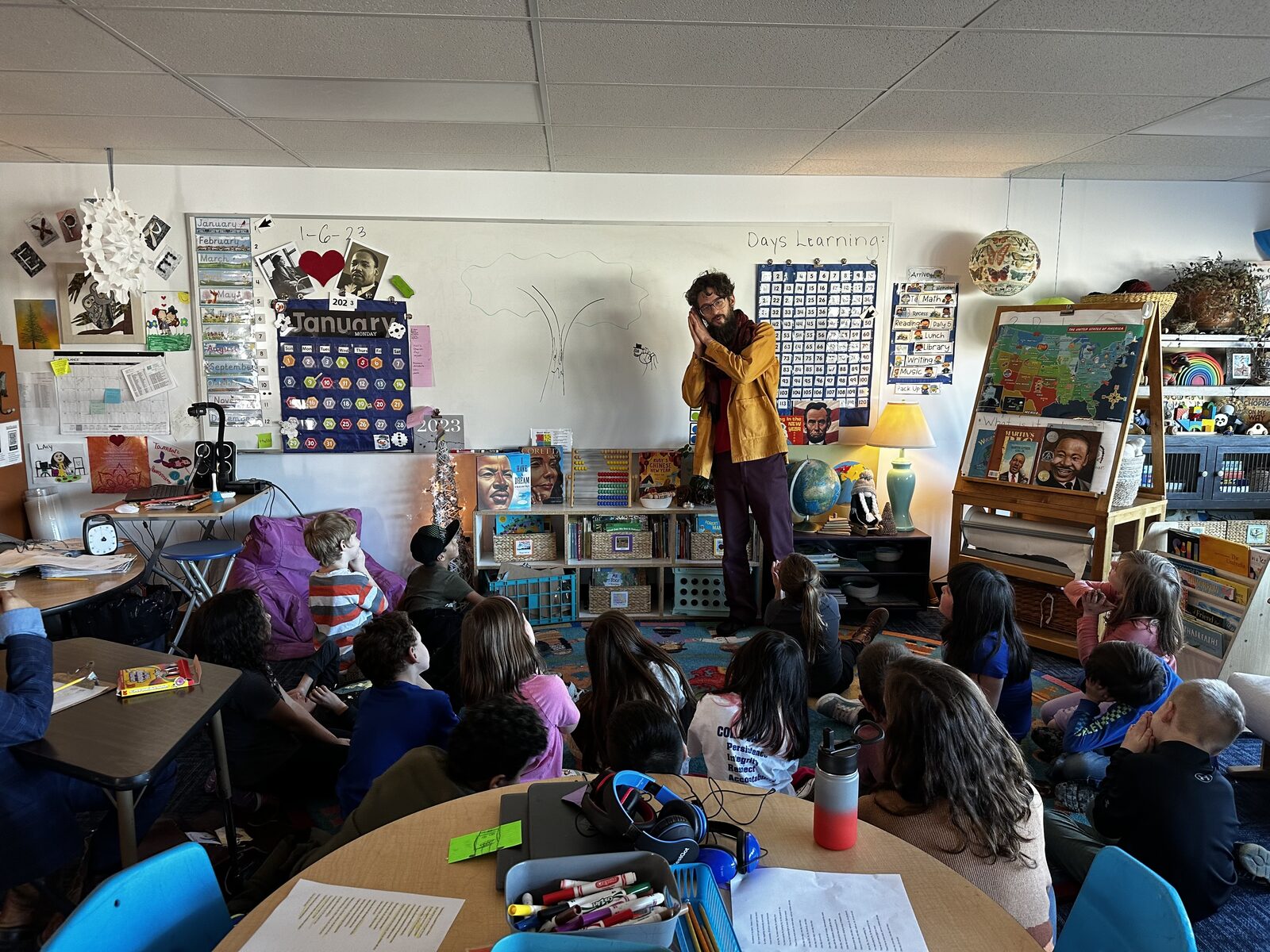 Travis leading a storytelling session, drawing a tree on the whiteboard for a circle of seated students